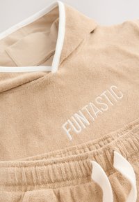Felpa con cappuccio beige realizzata in tessuto morbido e strutturato, con bordatura bianca e logo "FUNTASTIC" ricamato. Dotata di coulisse in vita.