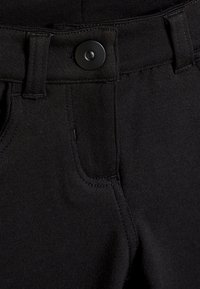 Pantaloni neri elasticizzati con chiusura a bottone, passanti per cintura e tasche laterali. Texture liscia con dettagli di cucitura minimi.