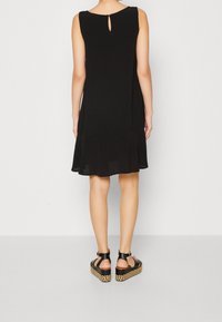 Robe noire sans manches avec un dos en trou de serrure et un ourlet évasé. Associée à des sandales à plateforme noires avec une semelle en paille tissée.