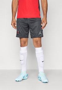 Hallid halli sportlikud lühikesed püksid vertikaalsete triipudega, Parisi logo ja Air Jordani embleem, koos valgete sokkidega ja helesiniste spordijalatsitega.