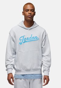 Lys grå hoodie med en frontlomme, der har et blåt broderet "Jordan" logo. Blødt stof, afslappet pasform og snoretræk ved hætten.