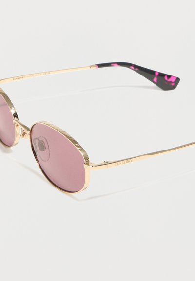 Οβάλ γυαλιά ηλίου με μεταλλικό χρυσό σκελετό, ροζ φακούς και μαύρες άκρες με έντονες ροζ πινελιές.