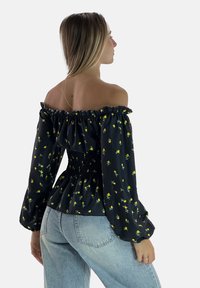 Schwarze, schulterfreie Bluse mit gerafftem Ausschnitt, Blumenmuster in Gelb und Grün, geraffte Taille, lange aufgebauschte Ärmel, getragen zu Jeans.