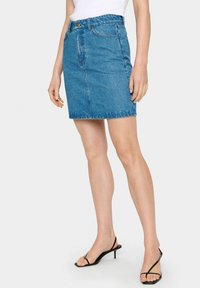 Denim mini sukňa v svetlom modrom odtieni, so strihom do rovna, prednými vreckami a detailmi prešívania. V kombinácii s čiernymi sandálmi na opätku.