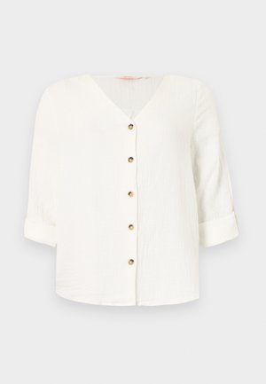 Blouse blanche texturée avec col en V, six boutons marron sur le devant, et manches trois-quarts retroussées sur un fond uni.