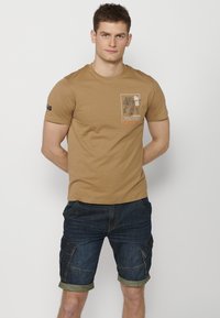 T-shirt en coton marron avec un design graphique représentant un tigre, associé à un short cargo en denim bleu foncé avec des manches retroussées et de multiples poches.