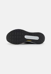 Semelle de chaussure noire avec un motif de crampons robuste, comportant une section centrale blanche et un logo "GOODYEAR" jaune, fabriquée en matériau en caoutchouc.