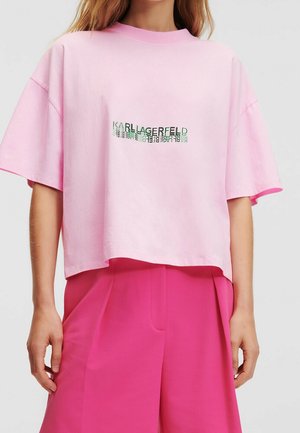 Donna che indossa una maglietta corta rosa con il testo "Karl Lagerfeld" specchiato e pantaloni ampi a vita alta di un vivace rosa.
