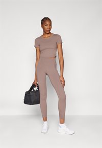 Light brown athletic set consisting of a fitted short-sleeve top and high-waisted leggings. Paired with white sneakers and a black gym bag.