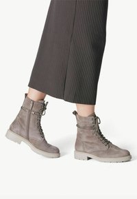 Bottines en daim gris avec lacets et fermeture éclair, présentant une surface texturée et une semelle en caoutchouc beige robuste.