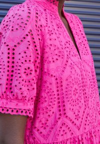 Rosa broderad klänning med korta puffärmar, med intrikata utskärningsmönster och hög krage, tillverkad av lättviktsmaterial.