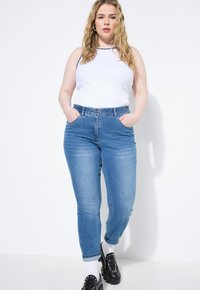 Světle modré džíny s polovičním pasem, zúženými nohavicemi a elastickým pasem. V kombinaci s bílým tílkem s černým lemem.