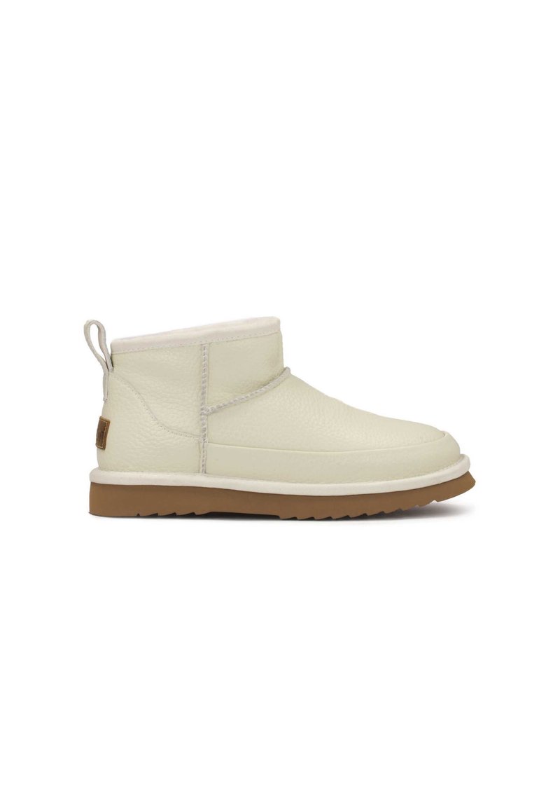 Botas de tobillo de cuero crema con un forro suave, suela de goma plana, punta redondeada y una lengüeta en la parte posterior para facilitar el uso.