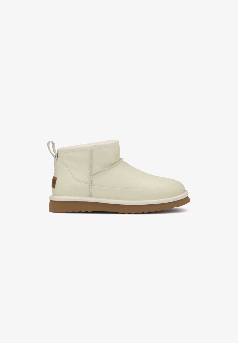 Botas de tobillo de cuero crema con un forro suave, suela de goma plana, punta redondeada y una lengüeta en la parte posterior para facilitar el uso.