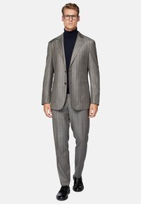 Costume gris à rayures fines avec un revers cranté, fermeture à un bouton et deux poches avant, associé à un col roulé bleu marine et des chaussures noires.