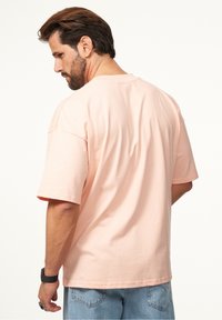 Rosa Kurzarm-T-Shirt aus weichem Stoff, mit lässiger Passform und Rundhalsausschnitt. Die Rückansicht zeigt ein nahtloses Design ohne sichtbare Logos.