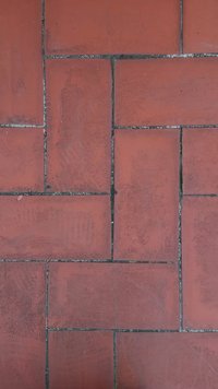 Piros agyagcsempék rácsos mintázatban elrendezve, látható textúrával és enyhe színeltérésekkel. Fugázó vonalak láthatók a csempék között.