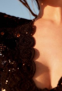 Zbliżenie na szyję i górną część klatki piersiowej osoby noszącej czarny szydełkowy strój z kwiatowymi wzorami w naturalnym świetle słonecznym.