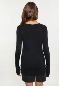 Pulover lung cu mâneci negre, cu un design ajustat, textură răsucită și nasturi decorativi la manșete. Material moale și decolteu tip echipaj.