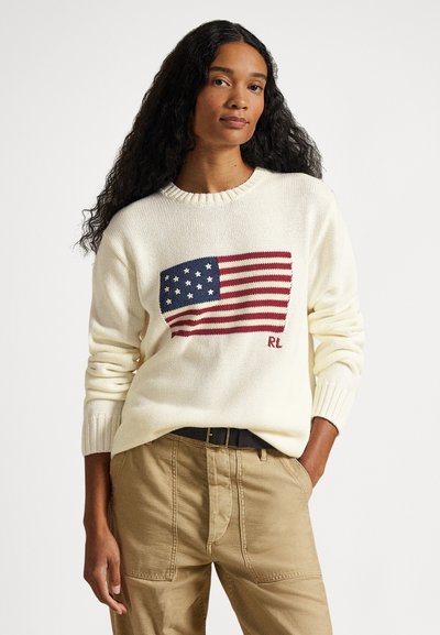 Ελαφρύ κρεμ πουλόβερ με πλεκτό σχέδιο της αμερικανικής σημαίας σε μπλε και κόκκινο. Διαθέτει ριμπ μανσέτες και στρογγυλή λαιμόκοψη. Φοριέται με χακί παντελόνια.