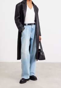 Svart läderjacka över en vit V-ringad tröja, ihop med ljusblå vida jeans, svart bälte och grova svarta stövlar, håller en svart väska.