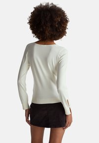 Bílý svetr s dlouhými rukávy a bočními rozparky, vyrobený z měkké, texturované látky. Má kulatý výstřih a přiléhavý střih.