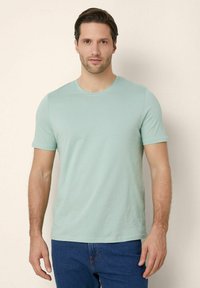 Tricou scurt de culoare verde deschis, dintr-un material moale, cu guler rotund. Purtați cu blugi albaștri, are un design ajustat și o textură netedă.