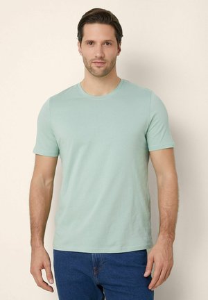 Tricou scurt de culoare verde deschis, dintr-un material moale, cu guler rotund. Purtați cu blugi albaștri, are un design ajustat și o textură netedă.