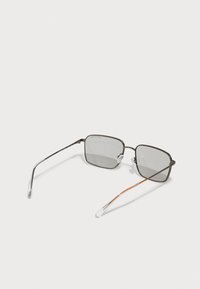 Ochelari de soare dreptunghiulari cu lentile gri, ramă subțire metalică de culoare maro, vârfuri transparente pentru braț și un accent subtil portocalie pe un braț.
