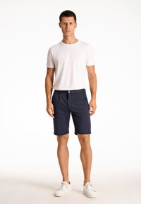 Navy shorts with a smooth texture and front pockets, paired with a fitted white short-sleeve t-shirt and white sneakers.