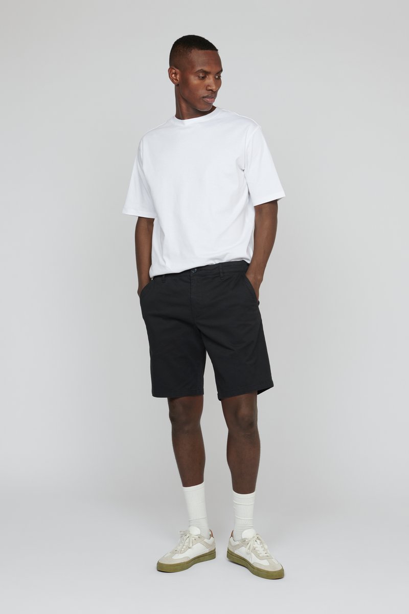 White short-sleeve t-shirt, black shorts, white socks, and sneakers. Casual outfit with a relaxed fit and minimal design.