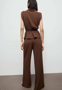 Hnedý pletený outfit, ktorý obsahuje top bez rukávov s rolákovým golierom a peplum pásom, doplnený širokými nohavicami a tenkým pásom.