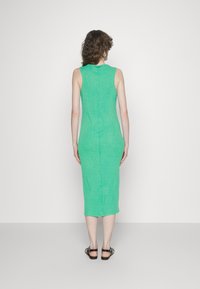 Vestido midi verde, sem mangas, de forma ajustada, com tecido texturizado, detalhe de zíper nas costas, cai um pouco abaixo do joelho, combinado com sandálias pretas.