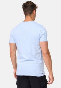 Camiseta de algodón azul claro con mangas cortas, escote redondo y detalles de costura lateral. Textura suave, diseño ajustado y sin gráficos.