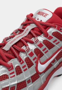 Červená a strieborná atletická obuv s priedušným materiálom, výrazným šnurovaním, bielym logom "swoosh" a polstrovaným jazykom s brandovaním "NIKE".