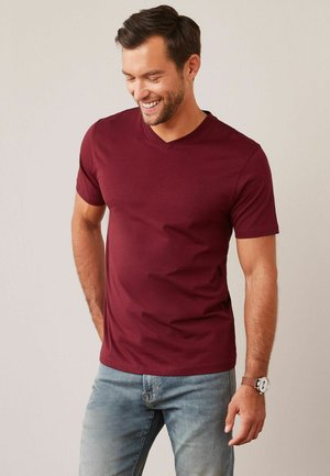 Bordeaux V-hals t-shirt van zachte stof, korte mouwen en een fitted silhouet, gecombineerd met lichtblauwe denim jeans.