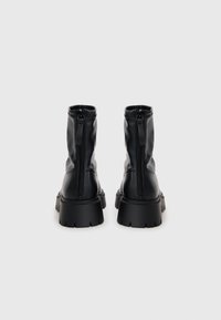 Zwarte enkellaarsjes met een soepele leren afwerking, achterste ritssluiting en robuuste rubberen zool met diepe groeven voor grip.