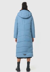 Light blue puffer coat with a hood and chevron quilting pattern, mid-length, featuring a branded patch at the hem and black ankle boots.