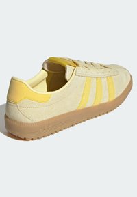 Kollane ja beeži mokassiin, millel on kolm kollast triipu, ümar nina ja kummist tald. Omab heledat kollast siseruumi ja tekstuurseid detaile.