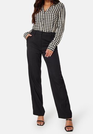 Mujer vistiendo una blusa de manga larga con estampado en blanco y negro, pantalones negros de cintura alta y tacones abiertos negros.