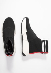 Černé nazouvací tenisky s pleteným svrškem, bílou stélkou, červenými akcenty a texturovanou gumovou podrážkou. Obsahují proužkované detaily na patě.