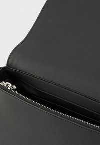 Μαύρη δερμάτινη τσάντα με απαλή υφή, με φερμουάρ και ασημένιες μεταλλικές λεπτομέρειες. Εσωτερικό εν μέρει ορατό.