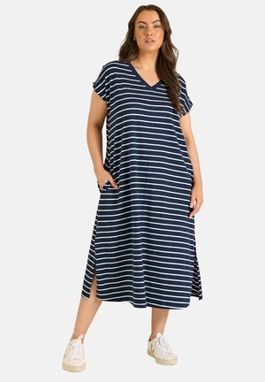 Frau im knielangen, marineblau-weiß gestreiften Kleid mit kurzen Ärmeln und seitlichen Schlitzen, kombiniert mit weißen Sneakers.