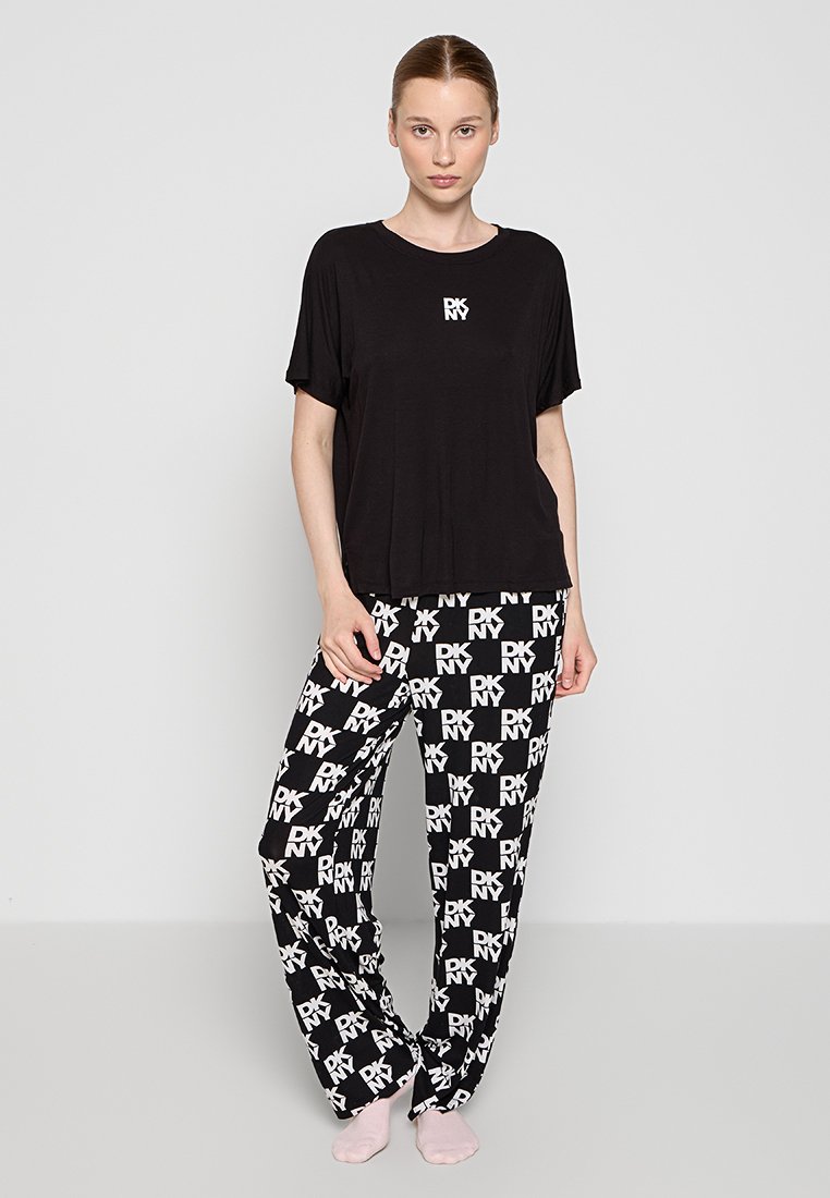 Czarny t-shirt z krótkim rękawem z białym logo, zestawiony z czarnymi spodniami w białą kratkę z tym samym logo.