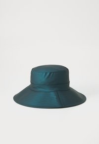 Türkisfarbene Bucket-Hat aus glattem, glänzendem Stoff. Verfügt über einen breiten, flexiblen Rand und ein genähtes Band um die Krone für zusätzlichen Detail.