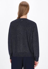 Pulover bleu marin cu o croială lejeră, tricot texturat și accente subtile din fir metalic. Detaliile cu manșete și tiv rib-knit accentuează structura.