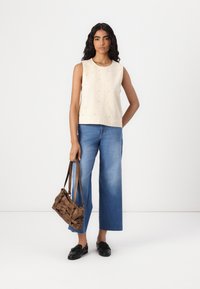 Top senza maniche di colore crema con decorazioni testurizzate, abbinato a jeans a gamba larga di un leggero blu. Una borsa marrone e mocassini neri completano l'outfit.