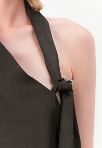 Mörkbrun topp med en asymmetrisk design, med en knuten rem och metalliskt detaljer vid axeln. Strukturerad tyg.