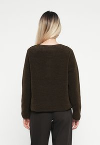 Brown fleece pullover with a textured surface, round neckline, and long sleeves. The design is relaxed-fit, featuring a straight hem.