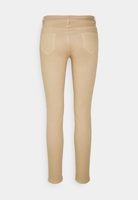 Jean skinny beige avec poches arrières et passants de ceinture. Texture lisse, tissu doux et coupe slim se rétrécissant à la cheville.